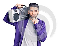 Young handsome man with beard listening to music using vintage boombox serious face thinking about question with hand on chin,