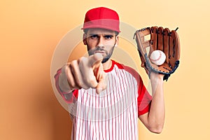 Young handsome man with beard playing baseball using ball and glove pointing with finger to the camera and to you, confident