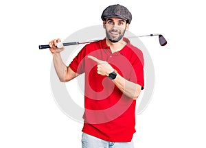 Young handsome man with beard playing golf holding club and ball smiling happy pointing with hand and finger