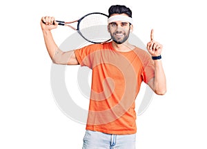 Young handsome man with beard playing tennis holding racket surprised with an idea or question pointing finger with happy face,