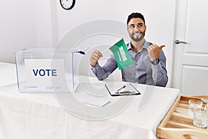 Young handsome man with beard at political campaign election holding arabia saudita flag pointing thumb up to the side smiling photo