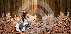 A young handsome man with a beard and shoulder-length hair, sits in a wild dense autumn forest.