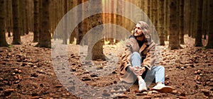 A young handsome man with a beard and shoulder-length hair, sits in a wild dense autumn forest.