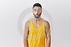 Young handsome man with beard standing over isolated background making fish face with lips, crazy and comical gesture