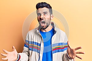 Young handsome man with beard wearing casual jacket crazy and mad shouting and yelling with aggressive expression and arms raised