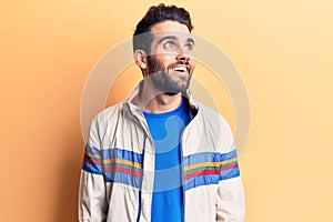 Young handsome man with beard wearing casual jacket looking away to side with smile on face, natural expression