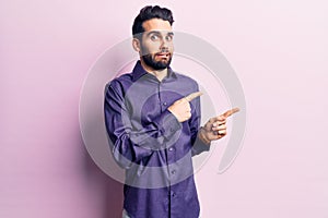 Young handsome man with beard wearing casual shirt pointing aside worried and nervous with both hands, concerned and surprised