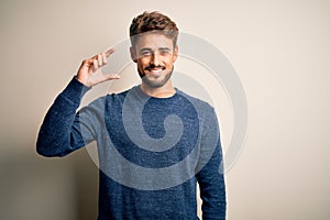 Young handsome man with beard wearing casual sweater standing over white background smiling and confident gesturing with hand