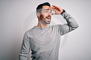 Young handsome man with beard wearing casual sweater standing over white background very happy and smiling looking far away with