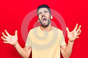 Young handsome man with beard wearing casual t-shirt crazy and mad shouting and yelling with aggressive expression and arms raised