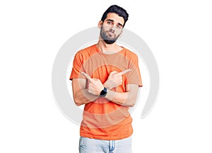 Young handsome man with beard wearing casual t-shirt pointing to both sides with fingers, different direction disagree