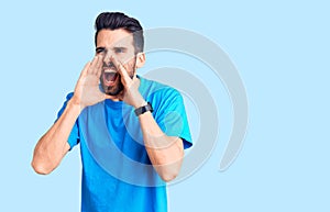 Young handsome man with beard wearing casual t-shirt shouting angry out loud with hands over mouth