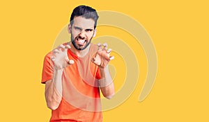 Young handsome man with beard wearing casual t-shirt smiling funny doing claw gesture as cat, aggressive and sexy expression