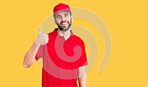 Young handsome man with beard wearing delivery uniform doing happy thumbs up gesture with hand
