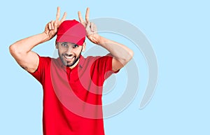 Young handsome man with beard wearing delivery uniform posing funny and crazy with fingers on head as bunny ears, smiling cheerful