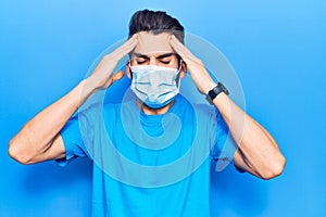 Young handsome man with beard wearing medical mask with hand on head, headache because stress