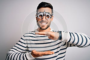 Young handsome man with beard wearing optometry glasses over isolated white background gesturing with hands showing big and large