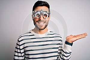 Young handsome man with beard wearing optometry glasses over isolated white background smiling cheerful presenting and pointing