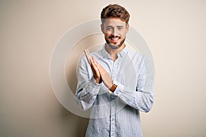 Young handsome man with beard wearing striped shirt standing over white background clapping and applauding happy and joyful,