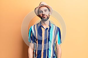 Young handsome man with beard wearing summer hat and shirt relaxed with serious expression on face