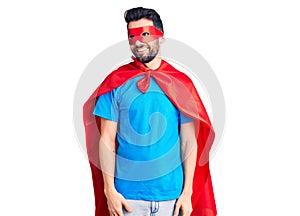 Young handsome man with beard wearing super hero costume looking away to side with smile on face, natural expression