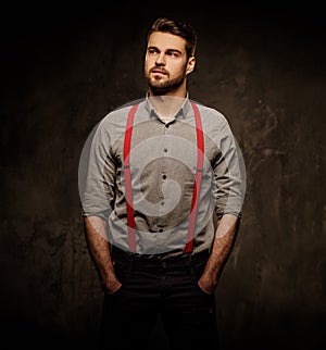 Young handsome man with beard wearing suspenders and posing on dark background.