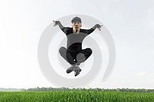 Young handsome man in black fashionable clothes in a stylish cap in trendy sneakers jumping on a background of green grass