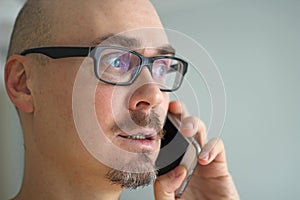 Young handsome man in black glasses is talking on the phone and smiling. Closeup portrait of a man. Manager, office worker,