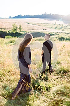 Young handsome man in black shirt and pants waiting for his pretty woman, standing in a field at summer sunset. Back