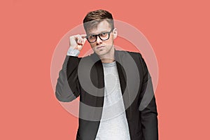 Young handsome man in black suit and glasses isolated on red background