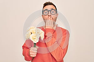 Young handsome man with blue eyes holding bouquet of flowers over white background cover mouth with hand shocked with shame for