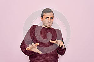 Young handsome man with blue eyes wearing casual sweater standing over pink background disgusted expression, displeased and