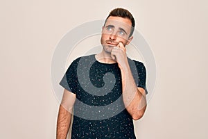 Young handsome man with blue eyes wearing casual t-shirt standing over white background with hand on chin thinking about question,