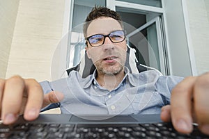 Young handsome man in a blue shirt is working at a computer on a light background. The programmer is focused on work