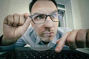 Young handsome man in a blue shirt is working at a computer on a light background. The programmer is focused on work. press the