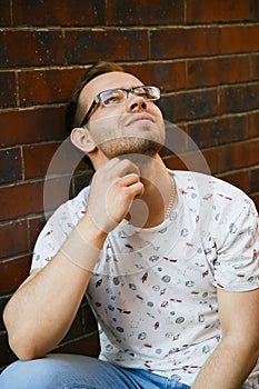 A young handsome man with bristles sits on a granite staircase near a brick building on a summer evening