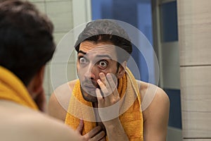 Young handsome man with bugged eyes looking at the mirror after morning routine in the bathroom