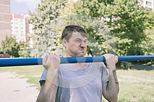 A young handsome man in casual clothes is doing pull up exercise on horizontal bar. fitness, sport, exercising, training
