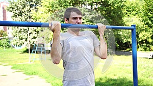 A young handsome man in casual clothes jokingly is doing pull up exercise on horizontal bar. The concept of humor, jokes