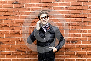 Young handsome man cell smart phone call speak smile over brick wall