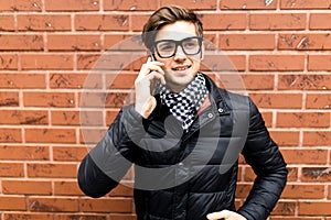 Young handsome man cell smart phone call speak smile over brick wall