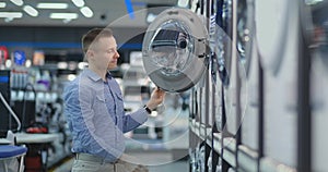 A young handsome man chooses a smart washing machine in a consumer electronics store for his new home. Studies the