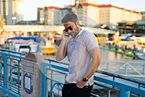 Young handsome man in classik polo t-shirt chatting on phone on the street. Handsome confident stylish hipster model