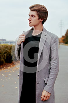 Young handsome man in coat. Portrait of fashionable well dressed man posing in grey stylish coat. Confident and focused boy