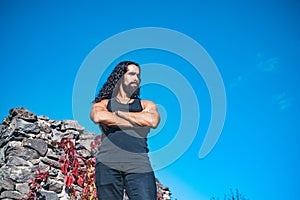 Young handsome man with crossed arms long hair beard, mustache and trendy hairdo outdoor.