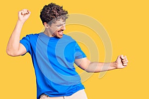Young handsome man with curly hair wearing casual clothes dancing happy and cheerful, smiling moving casual and confident