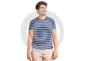 Young handsome man with curly hair wearing casual clothes looking away to side with smile on face, natural expression