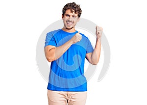 Young handsome man with curly hair wearing casual clothes pointing to the back behind with hand and thumbs up, smiling confident