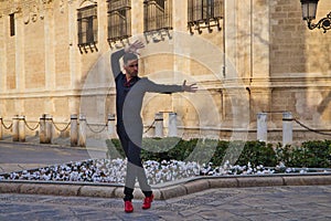 Young and handsome man dancing flamenco, dressed in black and wearing red shoes, is dancing in the street in the open air.