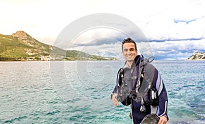 Young handsome man diver smiling ready to go scuba diving in cold water wet suit, fins, weight belt & oxigen gear in